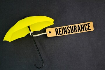 yellow umbrella and paper tag with the word REINSURANCE. insurance reform concept