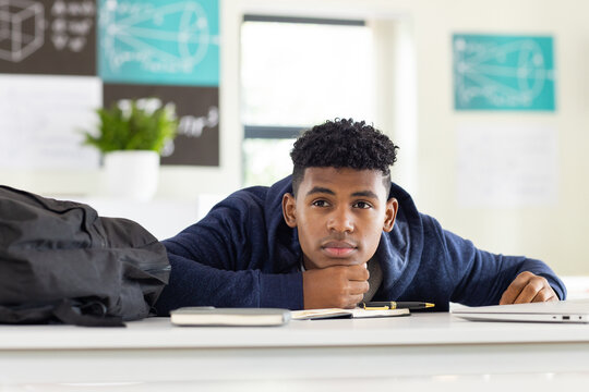 In school, African American teenage boy resting head on desk, looking thoughtful