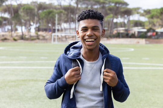 Smiling African American teenage boy standing on soccer field, enjoying outdoor time