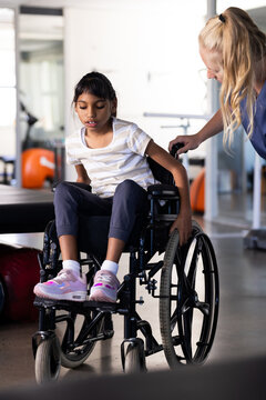 Assisting girl with cerebral palsy in wheelchair, female therapist during rehabilitation session