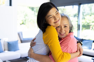 Asian woman hugging senior mother, smiling and enjoying time together at home