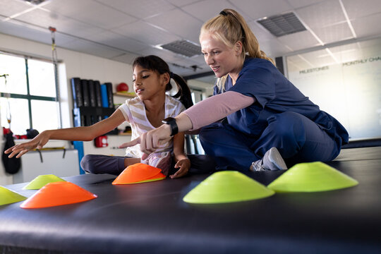 Female therapist guiding girl with cerebral palsy in physical rehab, using cones for therapy exercis