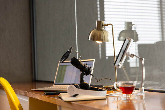 Podcasting setup with laptop, microphone, and headphones on desk, tea nearby, copy space