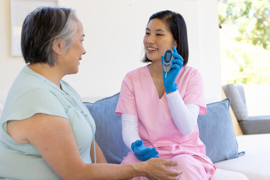 Female nurse in pink scrubs showing blood glucose meter to senior woman