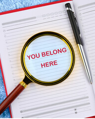 YOU BELONG HERE TEXT viewed through a magnifying glass in a business notebook