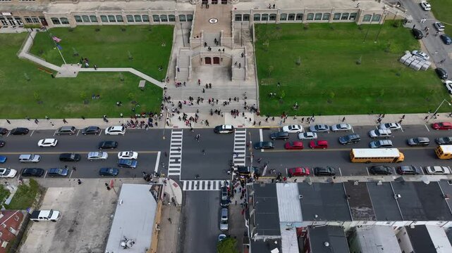 Students exiting American public school at dismissal. Police protecting school and buses transporting people. Aerial top down truck shot.