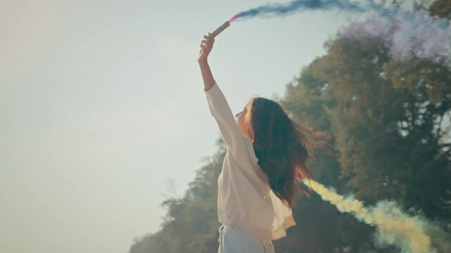 Happy asian woman with purple and yellow smoke bombs on the sea beach sunset, female activist portrait with active smoke grenades, freedom with playful dance spin slow motion