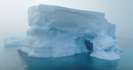 Towering melting iceberg drifting morning mist in Antarctica. Massive iceberg floating ocean in fog. Glacier melting, climate change impact on polar environment. Antarctic travel. Drone shot close up © mozgova