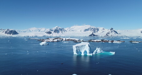 Iceberg drift in Antarctica ocean bay dark blue sea. The massive ice formation floats majestically in cold water. Mountain range in background. Sunny day. Expeditions and adventures. Aerial drone view