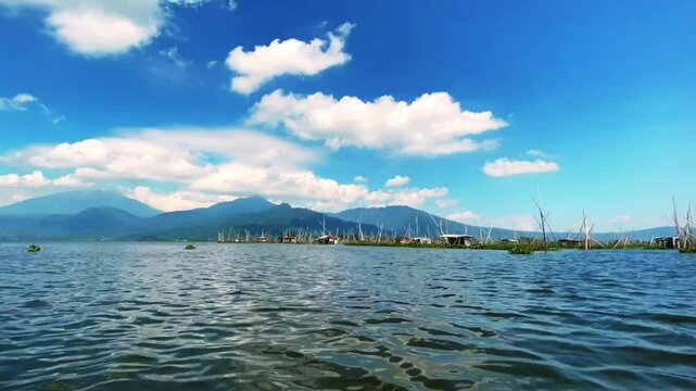Time lapse, Rawa Pening lake contains water hyacinth plants against a backdrop of mountains and blue sky and white clouds