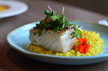 The plate features perfectly roasted cod with crispy skin, served on a vibrant Italian saffron risotto.
