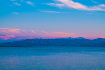 Germany, Orange sunset light on alps mountains nature landscape behind water of bodensee lake after sunset, panorama view from lindau to swiss coast and snow covered saentis peak