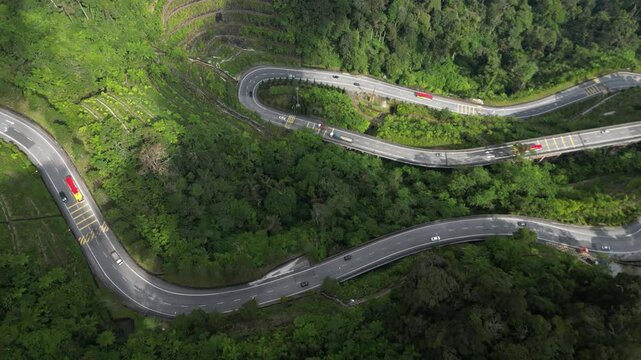 Drone flies over a road in the genting highlands malaysia - kurfen rich road with cars leads up the mountain