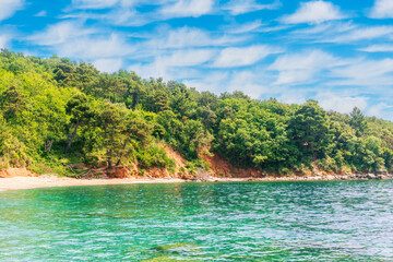 scenic summer landscape of beautiful sea shore with water vawes in bay, green forest on isle rock and nice cloudy sky on background