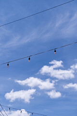 Light bulbs and power line with sky background in morning. Close-up hanging light bulbs and sky texture. Festival, landscape, travel, decoration concepts for wallpaper. Vertical sky with tidy clouds.