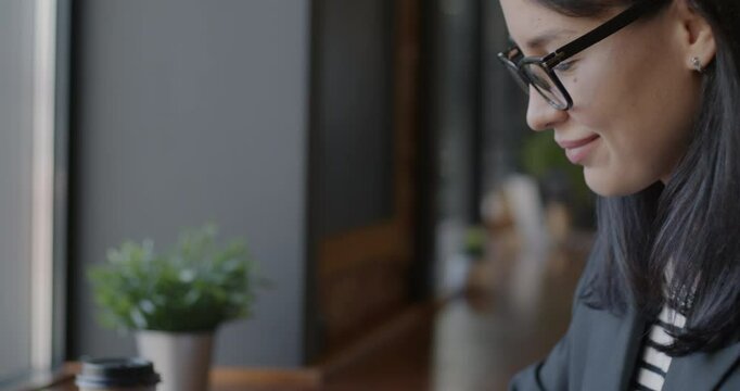 Close-up tilt-down portrait of young businesswoman typing with laptop computer at table in cafe. Modern technology and professional occupation concept.