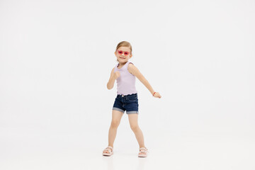 Little girl dancing in the studio on a white background. Happy energetic girl having fun and enjoying her childhood. Concept of fashion, style and happy children's emotions.