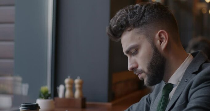 Slow motion tilt-down portrait of businessman writing in notebook and using laptop computer in cafe. Modern technology and business development concept.