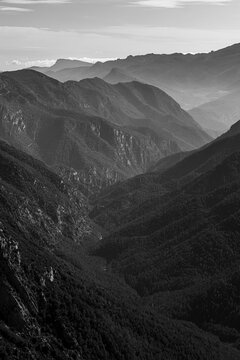 A stunning monochrome image that captures a vast and awe-inspiring mountain range, presenting layers of rugged peaks receding into the distance under a cloudy sky.