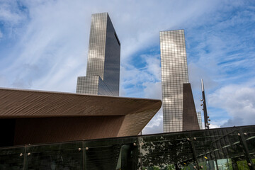 The image showcases two modern skyscrapers with a futuristic architectural design set against a backdrop of a partly cloudy sky, emphasizing urban development and progress in Rotterdam Netherlands