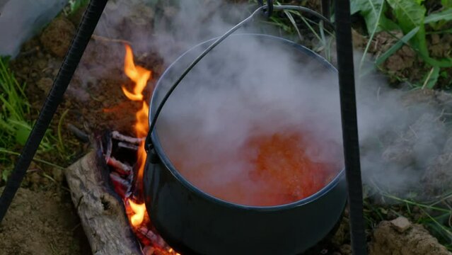 Close up with of boiling smoking stew in cauldron on fire