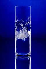 Traditional Turkish Raki glass with an artistic and dynamic splash of water inside, set against a vibrant blue background.