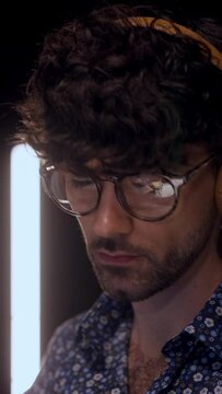 Curly eyeglasses man wearing headphones staring monitor while working online