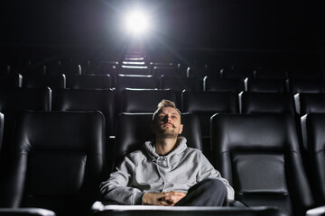 A man in a stylish hoodie attentively watches a movie at the cinema