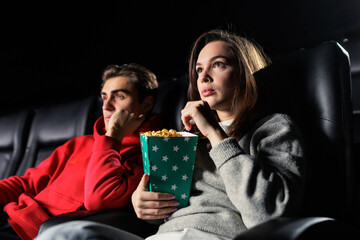 A close-up of a couple in love watching a movie at the cinema. Popcorn in the hands of a young woman