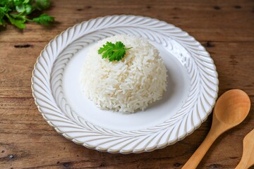 Cooked white rice or steamed rice in a white plate on wooden background, thai jasmine rice, thai fragrant rice, top view food table