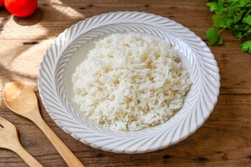 Cooked white rice or steamed rice in a white plate on wooden background, thai jasmine rice, thai fragrant rice, top view food table