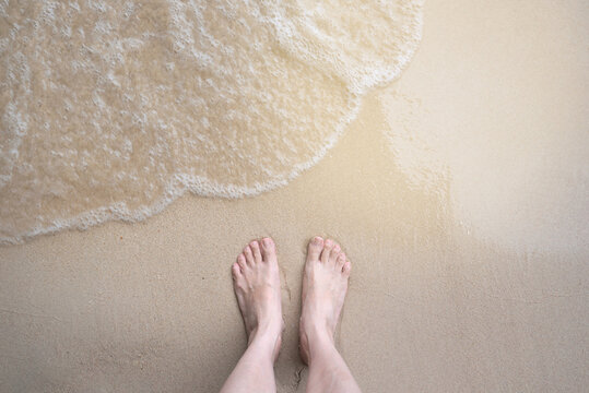 Woman feet standing on sand beach with her bare feet at the sea. Naked feet at the beach with wave on vacation. Barefeet nature background concept, copy space. 