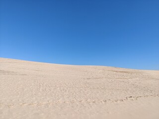 Empty sand dune with footprints and clear, blue sky horizon without clouds