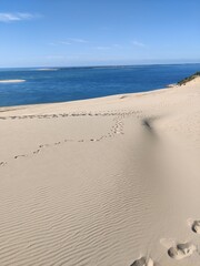 Sand dune with wind pattern and footprints with dark blue sea in the background