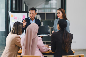 Diverse business team analyzing data and discussing strategies during an office meeting, using documents and a laptop.