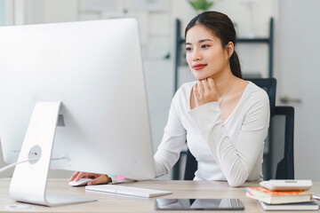 Smiling woman working on desktop while sitting in comfortable home office with notebook and...