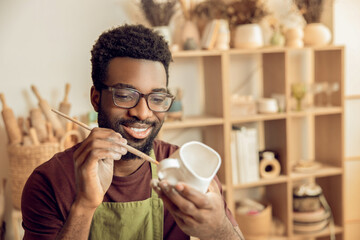 Male sculptor brushing the clay mug and looking involved