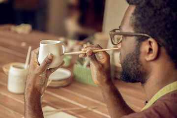 Male sculptor brushing the clay mug and looking involved