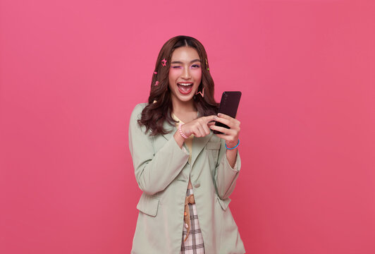 Young smiling happy asian woman 20s using mobile cell phone wow face looking isolated on pink copy space background.