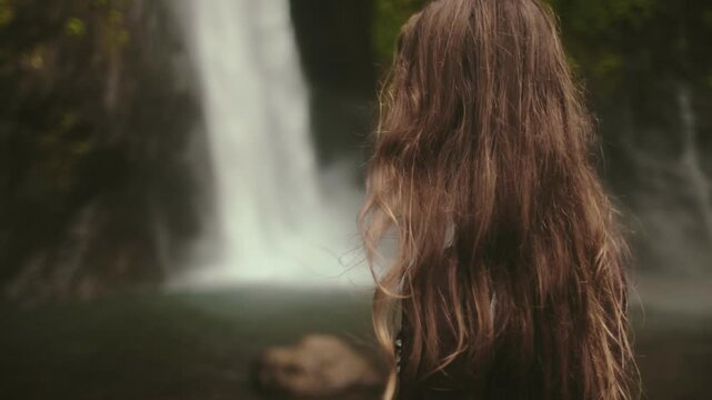Beautiful woman standing against powerful Bali waterfall. Travel, tourism, holiday, freedom and active lifestyle concept. Indonesia, Bali island, Air Terjun Munduk, Melanting Waterfalls. Slow motion