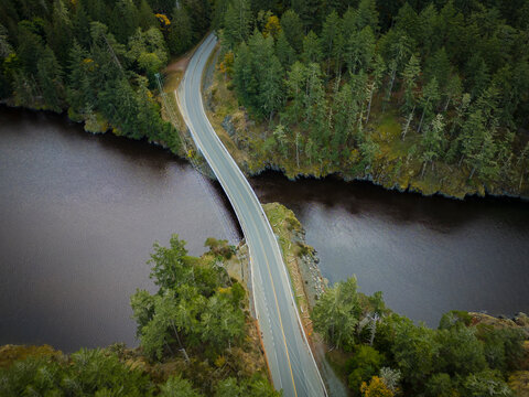 Aerial view of winding road and bridge through lush forest, Sooke, British Columbia, Canada.