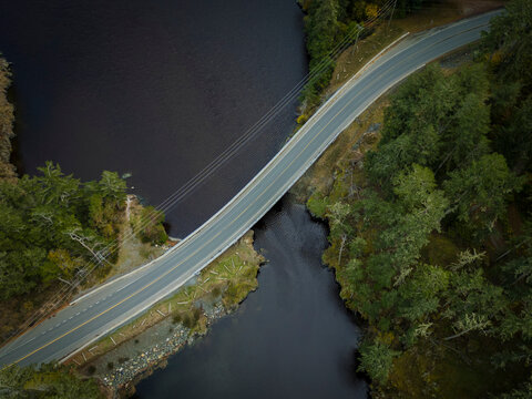 Aerial view of serene lake, winding road, and tranquil bridge surrounded by forest, Sooke, British Columbia, Canada.
