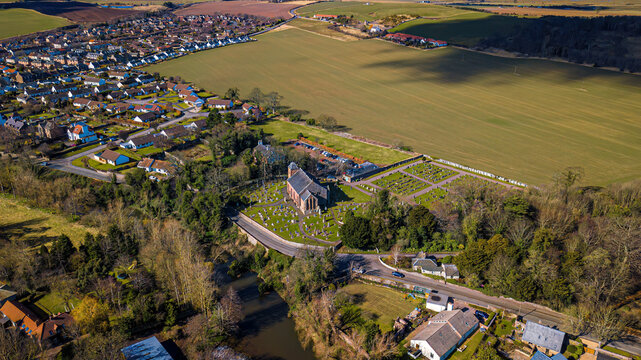 Aerial view of Prestonkirk Church and village surrounded by fields and homes, East Linton, Scotland.