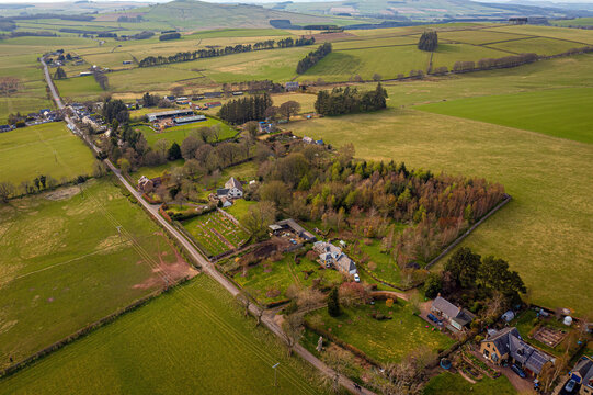 Aerial view of peaceful village life surrounded by fields, trees, and houses in Chesters, Hawick, Scotland, United Kingdom.