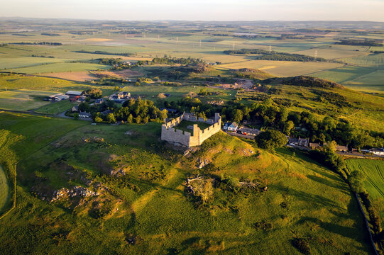 Aerial view of Hume Castle surrounded by fields, village, and buildings, Scottish Borders, United Kingdom.