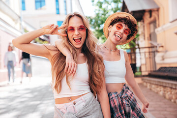 Two young beautiful smiling hipster female in trendy summer white t-shirt and shorts clothes. Sexy carefree women posing in street. Positive models having fun, hugging and going crazy, show peace sign