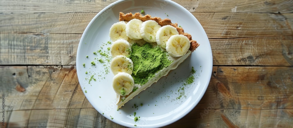 Poster banana-topped matcha banoffee pie on a white plate with a wooden table backdrop for a copy space ima