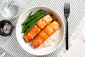 Top view of homemade lunch. Honey, orange juice garlic glazed roasted salmon fish with long rice and green beans in a white plate, white and grey linnen runner.