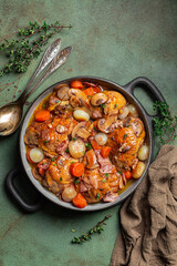 Coq au vin or rooster, cock with wine.  French dish of chicken braised with red wine, lardons, mushrooms, carrot and onion. Seasoned with salt, pepper, thyme. Green table surface. Vertical image.