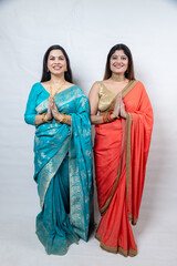 Fototapeta premium Two happy indian women greeting, join hands do namaste standing in saree, Isolated over white background. Culture of india.